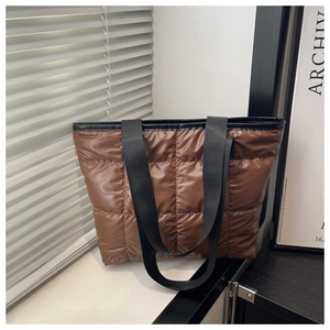 Detail of a brown quilted down tote bag with wide black nylon straps in natural light