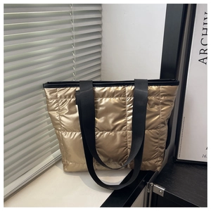 Close-up of golden quilted tote bag with metallic finish and wide black nylon shoulder straps