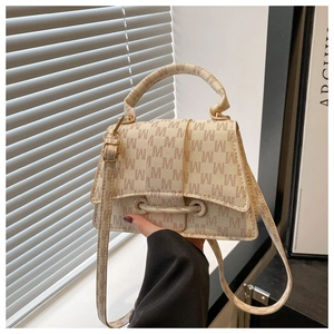 Close-up of cream handbag featuring M-letter pattern and golden hardware under natural light