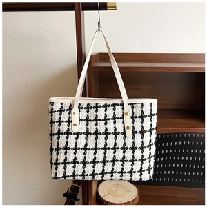 Detail of tweed tote bag showing black and white checkered fabric and leather handle with rivets