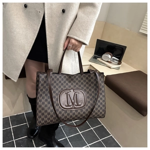 Close-up of a brown tote bag with M-letter print and large embossed logo on a model