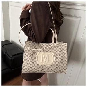 Detail of monogram M print tote bag with embossed leather logo patch on textured fabric
