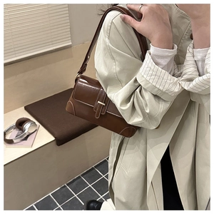 Detailansicht der braunen glänzenden Schultertasche mit Goldschnalle und Ziernaht