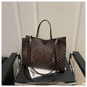 Detail of large tote bag with brown M letter print and logo on modern chair