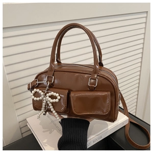 Detail of a shiny brown Boston bag featuring pearl bow charm and twin front pockets