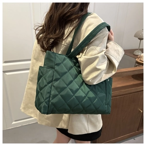 Detailed side view of deep green quilted tote bag with side pocket on a model's shoulder