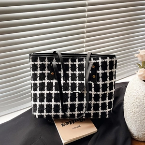 Large black and white houndstooth tweed tote bag with leather handles on a black blazer