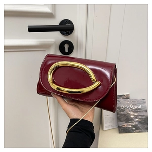 Detail of burgundy patent leather handbag featuring a large gold oval metal handle