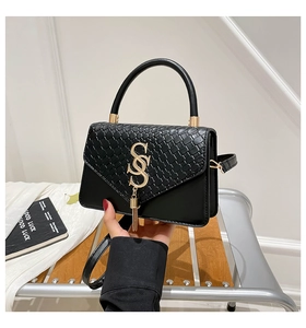 Detail of black woven leather handbag with gold S logo and fringe pendant accessory