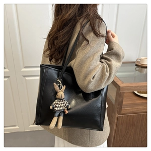 Detail of a large black leather tote bag with a checkered bunny charm for casual commuting