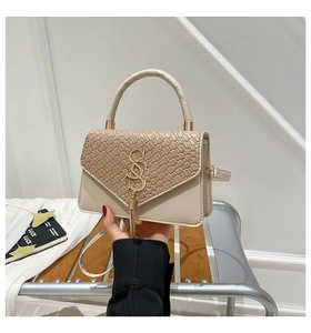 Close-up of beige woven texture handbag with gold logo clasp and long tassel pendant