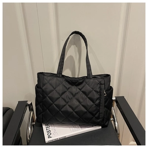 Detail of black quilted tote bag showing large diamond stitching and side gold zipper