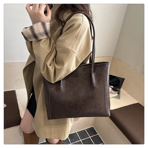 Retro large coffee tote bag in matte leather texture shown on shoulder with trench coat