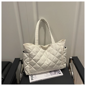Close-up of a white quilted tote bag with diamond stitching on a black chair