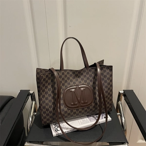 Dark brown tote bag with letter prints and a large round M logo on a stylish chair