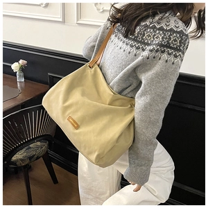 Detail of a beige canvas tote bag with brown leather handles and yellow logo tag
