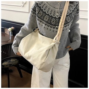 Close-up of minimalist cream tote bag with adjustable strap and gold metal hardware logo