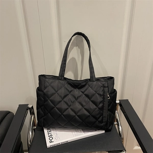 Black quilted tote bag with diamond pattern and long straps on a leather chair