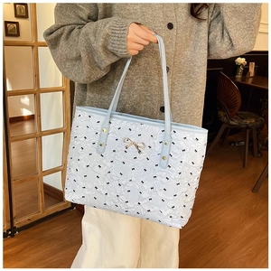 Sac fourre-tout bleu clair à imprimé nœuds noirs et boucle dorée tenu par un mannequin