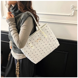 Détail du sac cabas blanc avec imprimé nœuds noirs et accessoire en métal doré