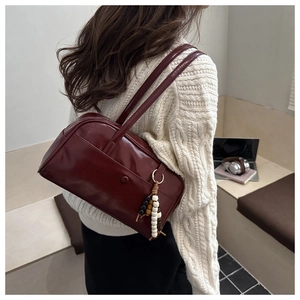 Detail of burgundy glossy shoulder bag with decorative beaded charm and outer snap pocket
