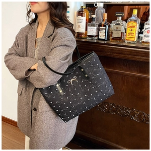 Détail du sac cabas à pois avec un nœud doré sur un tissu plissé et brillant
