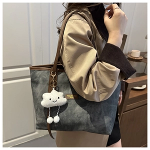 Detail of grey tote bag with brown leather trim and a white plush cloud charm accessory