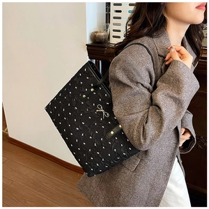Détail du sac cabas matelassé noir avec breloque nœud doré et poignées en cuir renforcé