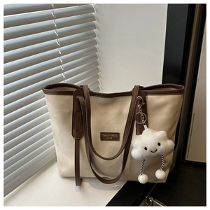 Detail of beige canvas tote bag with brown leather trim and a cute cloud plush charm
