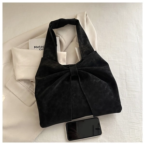 Détail du sac cabas en daim noir avec un nœud papillon à côté d'un téléphone intelligent