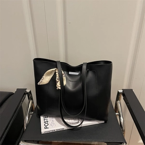 Large vintage black tote bag with silk scarf detail on a modern minimalist chair