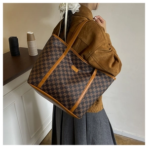 Close-up of brown checkered tote bag with leather handles shown on shoulder