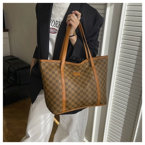 Detail of a large brown geometric pattern tote bag worn by a model in a minimal setting