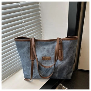 Close-up of retro washed blue denim tote bag featuring brown leather trim and brand logo
