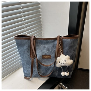 Detail of blue denim tote bag with brown leather handles and a white cloud plush charm