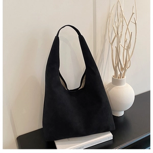 Close-up of a matte black suede hobo tote bag on a minimalist display with white decor