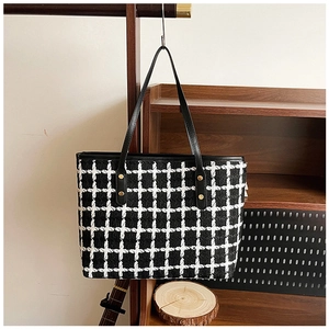 Detail of checkered woven tote bag with black leather handles and gold rivet accents