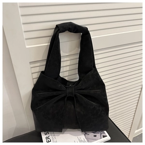 Detail of a black suede tote bag featuring a large decorative bow on a sleek bench