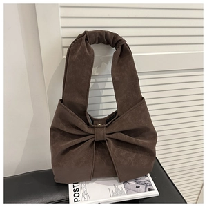 Detail view of the deep brown suede tote bag with oversized bow design on a bench