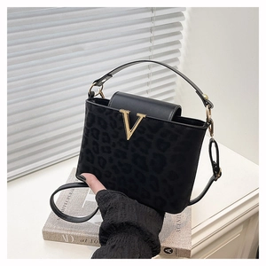 Detalle de bolso bandolera de leopardo negro con hebilla en V dorada y textura de gamuza