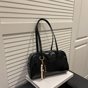 Glossy black vintage shoulder bag with beaded charm on a retro chair setting