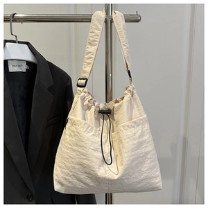 Detail of cream nylon tote bag featuring adjustable black straps and drawstring closure
