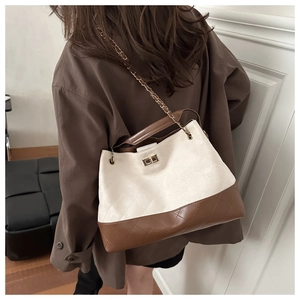 Detail of quilted suede tote with gold chain strap and turn-lock on a brown coat
