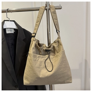 Detail of beige nylon crossbody bag featuring drawstring closure and black strap