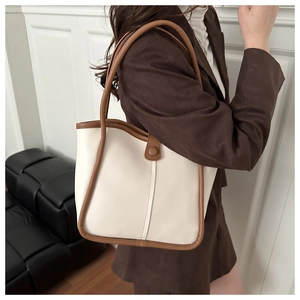 Detail of a large cream tote bag with brown leather trim worn by a model in a modern room