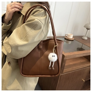 Detail view of brown leather underarm tote with a white plush eye charm on a trench coat