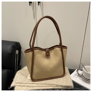 Close-up of minimalist beige tote bag with brown leather piping on a soft knit blanket