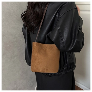 Brown matte suede bucket bag worn over a black leather jacket with a minimalist style