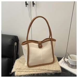 Detail of minimalist cream leather bucket bag with brown contrast trim and button closure