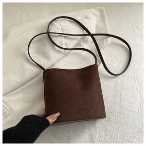 Detailed view of dark brown faux suede texture and long shoulder strap on a bucket bag